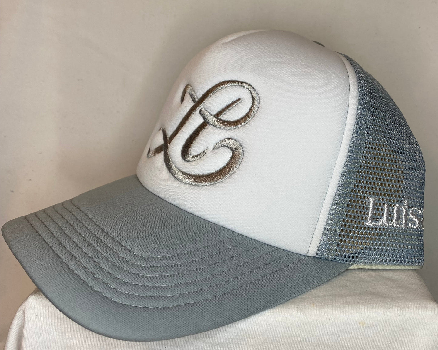 White and gray cap with embroidered design on a beige background